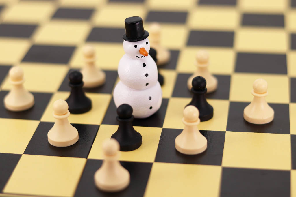 Ein Schachspiel mit einem Schneemann auf dem Feld. Der Schneemann wird von ettlichen Bauern in weiß und schwarz umkreißt.